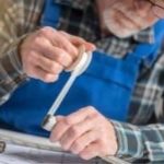 A man in a blue apron using a measuring tool with architectural plans on the table, focused on craftsmanship.