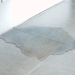 Water puddle on tiled floor indicating potential slab leak risks for RupCoe Plumbing services.