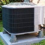 Air conditioning unit on grass showcasing black and silver components, maintained for summer efficiency by RupCoe Plumbing.