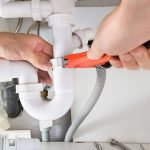 Close-up of hands using an adjustable wrench on white plumbing pipes for maintenance at RupCoe Plumbing.