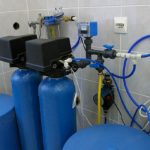 Blue water treatment tanks with piping and control panel, essential for home water filtration system by RupCoe.