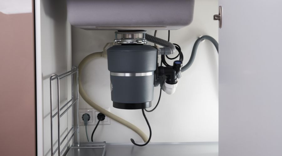 Garbage disposal unit under kitchen sink with gray finish and plumbing by RupCoe Plumbing.