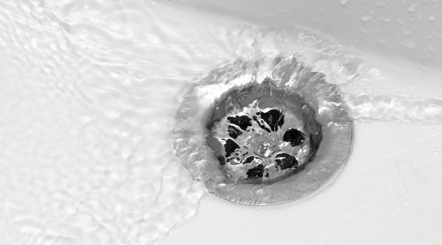 Water flowing into a shiny metal drain, illustrating plumbing and drain cleaning services related to residential issues.