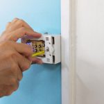 Person installing a programmable thermostat on a wall, demonstrating professional HVAC installation for improved energy efficiency and comfort management.
